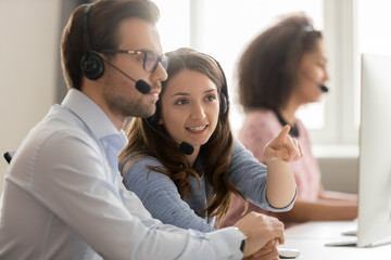 Female worker in headset help colleague with pc