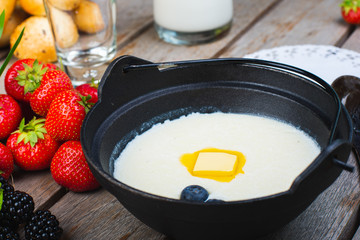 Traditional breakfast milk porridge with butter and berries on a wooden table.