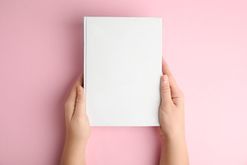 Woman holding book with blank cover on pink background, top view