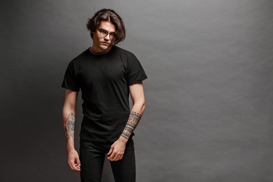 Hipster handsome male model with glasses wearing black blank t-shirt and black jeans with space for your logo or design in casual urban style