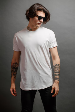 Hipster handsome male model with glasses wearing white blank t-shirt and black jeans with space for your logo or design in casual urban style