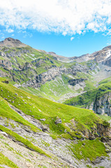 Vertical picture of amazing Alpine landscape photographed on a sunny day. Green pastures on rocky mountains. Beautiful Swiss landscape in Kandersteg area, above Oeschinensee. Switzerland in summer