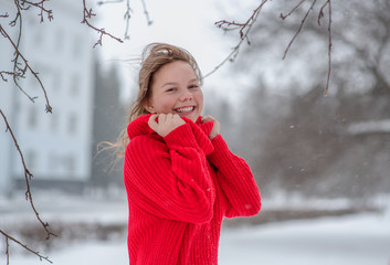 teen girl standing in the snow in the winter in the red sweater
