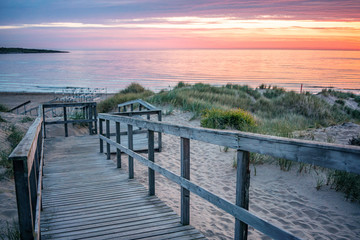 Wooden path at Baltic sea over sand dunes with ocean view, sunset summer evening