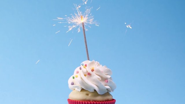 Birthday cupcake with sparkler on light blue background. Slow motion effect