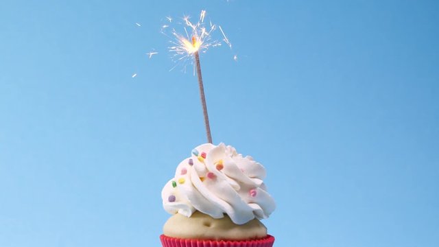 Birthday cupcake with sparkler on light blue background. Slow motion effect