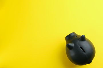 Black piggy bank on yellow background, top view. Space for text
