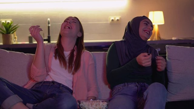 Multicultural friends watching comedy show on tv, laughing at joke together