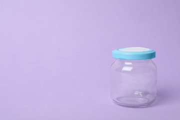 Closed empty glass jar on lilac background, space for text