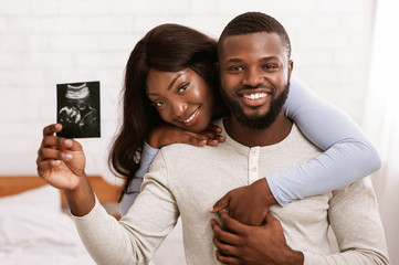 Fototapeta premium Cheerful married couple holding ultrasound image of their baby
