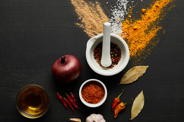 Top view of onion with garlic, olive oil and spices on black wooden background