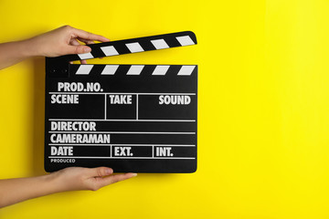 Woman holding clapperboard on yellow background, closeup with space for text. Cinema production
