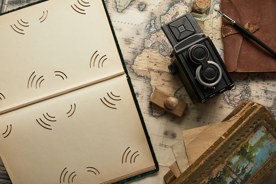 top view of vintage camera, notepad with fountain pen, empty photo album and painting on map background
