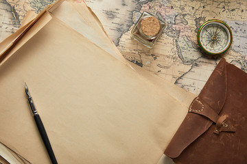 top view of vintage blank paper with fountain pen near compass and leather notepad on map background