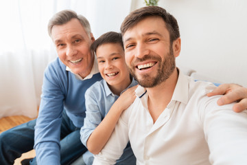 Man with son and father making selfie sitting on sofa