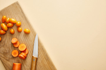 Top view of carrot and cherry tomatoes with knife on cutting board on beige background