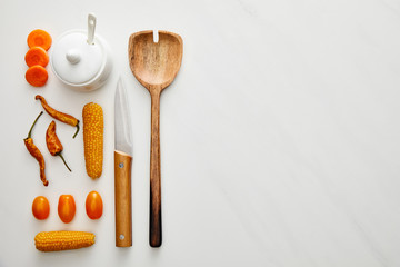 Top view of wooden spoon with knife and vegetables on marble background