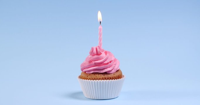 Birthday cupcake with burning candles on light blue background