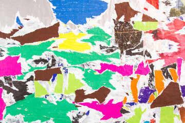 Torn and peeling pieces of paper posters on billboard with rough surface texture background.