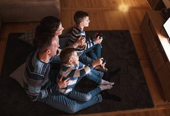 Parents with the children sitting at home on a pleasant evening and playing games on console. They...