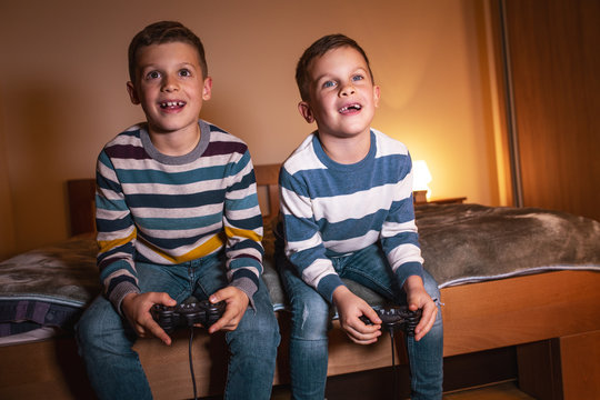 Two little brothers sitting at home on pleasant evening and playing games on console.They challenge each other to win .