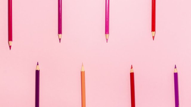 Stop motion animation red, pink, purple, and orange pencils move forward two at time at the top and battom clap their teeth flat lay top view on crayon background with copy space. 