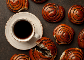 coffee and a lot of buns with poppy seeds on a stone background