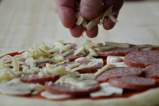 vMan's hand puts cheese, mozzarella on pizza. The process of cooking an Italian dish.