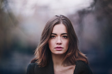 Attractive charming young woman in a dark coat walking in the autumn park. Cloudy. Soft colors of nature. The melancholy mood.