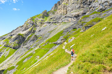 Hiking path in the Swiss Alps photographed in the summer season. Hikers walking the trail in Kandersteg area, Switzerland. Steep mountains in the background. Green Alpine landscape