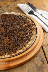 Brigadeiro pizza with grinded chocolate, fork and knife over wooden table