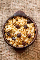 Sweet millet porridge with dark raisins in ceramic rustic bowl. Flat lay, top view