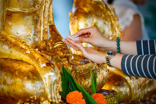 A young girl decorates a statue of Buddha in gold foil in a temple