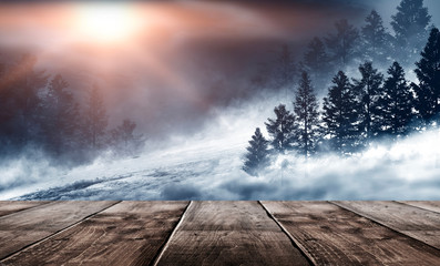 Winter background. Winter snow landscape with wooden table in front. Dark winter forest background at night. Snow, fog, moonlight. Dark neon night background in the forest with moonlight.