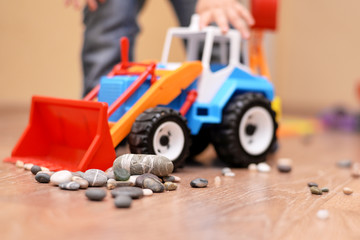 Colorful toy tractor with stones on the floor in the room.
