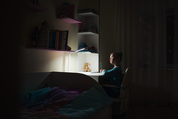 cute 7 y.o. girl doing homework  with table lamp in dark room