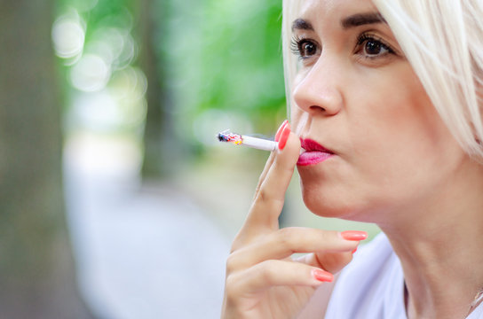 A woman smokes a cigarette. Holds in the mouth, red lips