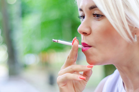 A woman smokes a cigarette. Holds in the mouth, red lips