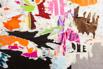 Torn and peeling old shabby gloss paper placards and posters layers on rough surface texture...