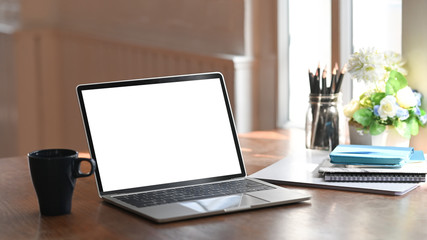 Empty screen laptop computer, notebook, pencil holder with flower and coffee cup on wood table.