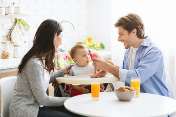 Obraz na płótnie Canvas Happy millennial parents feeding baby boy at kitchen