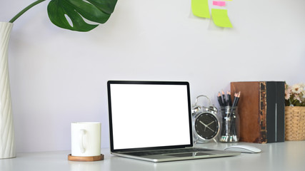 Mockup laptop computer on workspace with books, coffee, pencil holder and alarm clock.