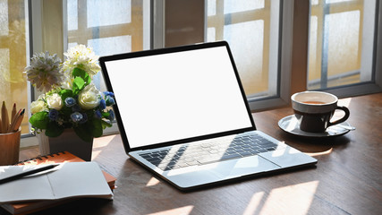 Empty screen laptop computer, creative supplies and hot tea on table near a windows.