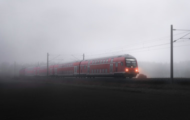 Passenger train moving through fog landscape. Red train and mist