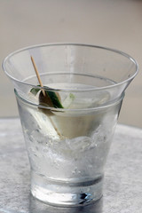 Glass of clear alcoholic drink with olive, lime peel and ice cubes.Close-up of glass with ice cubes, olive and lime