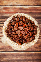 Freshly roasted aromatic coffee in a burlap bag on a wooden background.