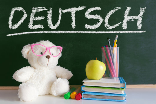 Hand writing on a blackboard in a language class for children with the word "English" writen on. Some books and school materials.