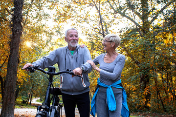Mature couple woman and man with bicycle walking in the park and talk