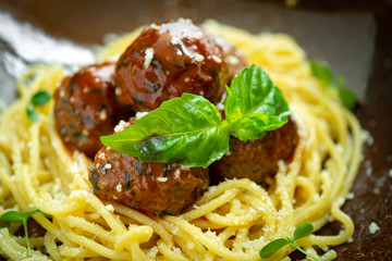 Spaghetti pasta and meat balls in tomato sauce in brown plate with Basil and Parmesan on wooden background. Rustic style