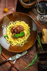Spaghetti pasta and meat balls in tomato sauce in brown plate with Basil and Parmesan on wooden background. Rustic style